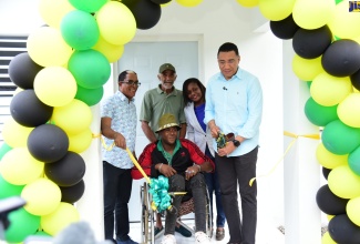 Prime Minister, the Most. Hon. Andrew Holness (right), cuts the ribbon to officially hand over a new two-bedroom home in Belfield, St. Mary, to beneficiary Davis Morris (second left) under the New Social Housing Programme, in Belfield, St. Mary, on Thursday (December 21).  Looking on are son of the beneficiary, Calvin Morris (in wheelchair); Minister of State in the Ministry of Labour and Social Security and St. Mary South Eastern Member of Parliament, Dr. the Hon. Norman Dunn; and Permanent Secretary in the Ministry of Economic Growth and Job Creation, Arlene Williams.