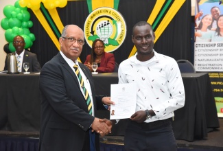 Chief Executive Officer, Passport , Immigration and Citizenship Agency (PICA), Andrew Wynter (left), presents a Certificate of Citizenship to newly minted Jamaican, Richardson Louis, during PICA’s citizenship ceremony at The Jamaica Pegasus hotel in New Kingston, on Monday (December 4)

