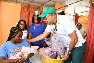 Minister of Health and Wellness, Dr. the Hon. Christopher Tufton, greets Tiffany Broodie, mother of Arielle Rhoden, who was one of several babies delivered at the Victoria Jubilee Hospital (VJH) in Kingston on Christmas Day (December 25). The newborn, who weighed 2.80 kilogrammes (approximately 6.17 pounds), arrived at 8:17 a.m. Dr. Tufton, who visited the hospital, presented Ms. Broodie with a gift basket containing personal care items courtesy of the Cari-Med Group/Kirk Distributors Limited. Sharing the moment are Promoter, Cari-Med/Kirk Distributors, Marlene Wright (second left); and Matron at VJH, Elise Fairweather.