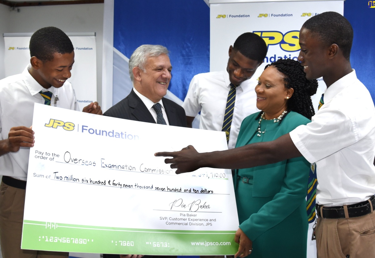 Deputy Chief Education Officer, Curriculum and Services Division, Ministry of Education and Youth, Dr. Clover Hamilton-Flowers (second right), looks at a symbolic cheque valued at more than $2.6 million, representing grant funding by the Jamaica Public Service Company (JPS) towards Caribbean Secondary Education Certificate (CSEC) Industrial Technology (Electrical) examinations for academic year 2023/2024. She is joined by (from left) Kingston High School student, Bently Mills; Clarendon College student, Austin Wright, and Brandon Levy also of Kingston High. Chairman of JPS, Damian Obiglio (second left), made the presentation during a ceremony held at the company’s offices in New Kingston on December 5.