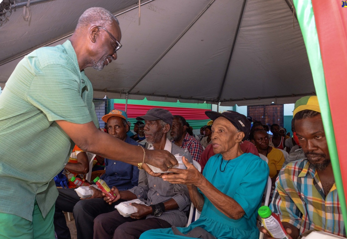 Minister of Local Government and Community Development, Hon. Desmond McKenzie (left), hands a meal to an elderly resident during Wednesday’s (December 20) annual West Kingston Senior Citizens’ Treat held at the Tivoli Gardens Community Centre in Kingston. 

