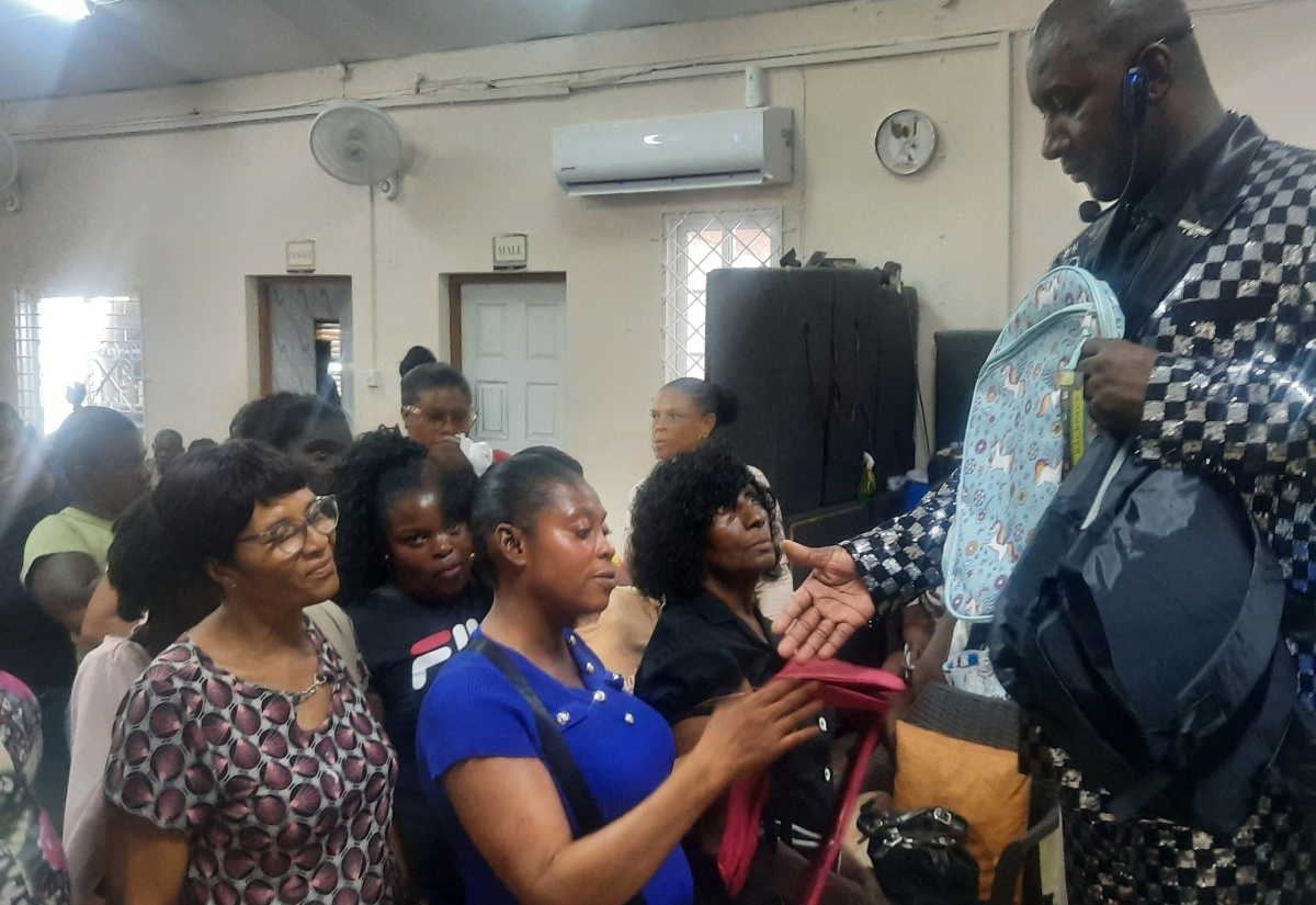 Founder of the Power of God Ministries International (PGMI), Prophet Roydel Rowe (right), hands over school bags to parents at the church, in Mandeville, Manchester, recently.