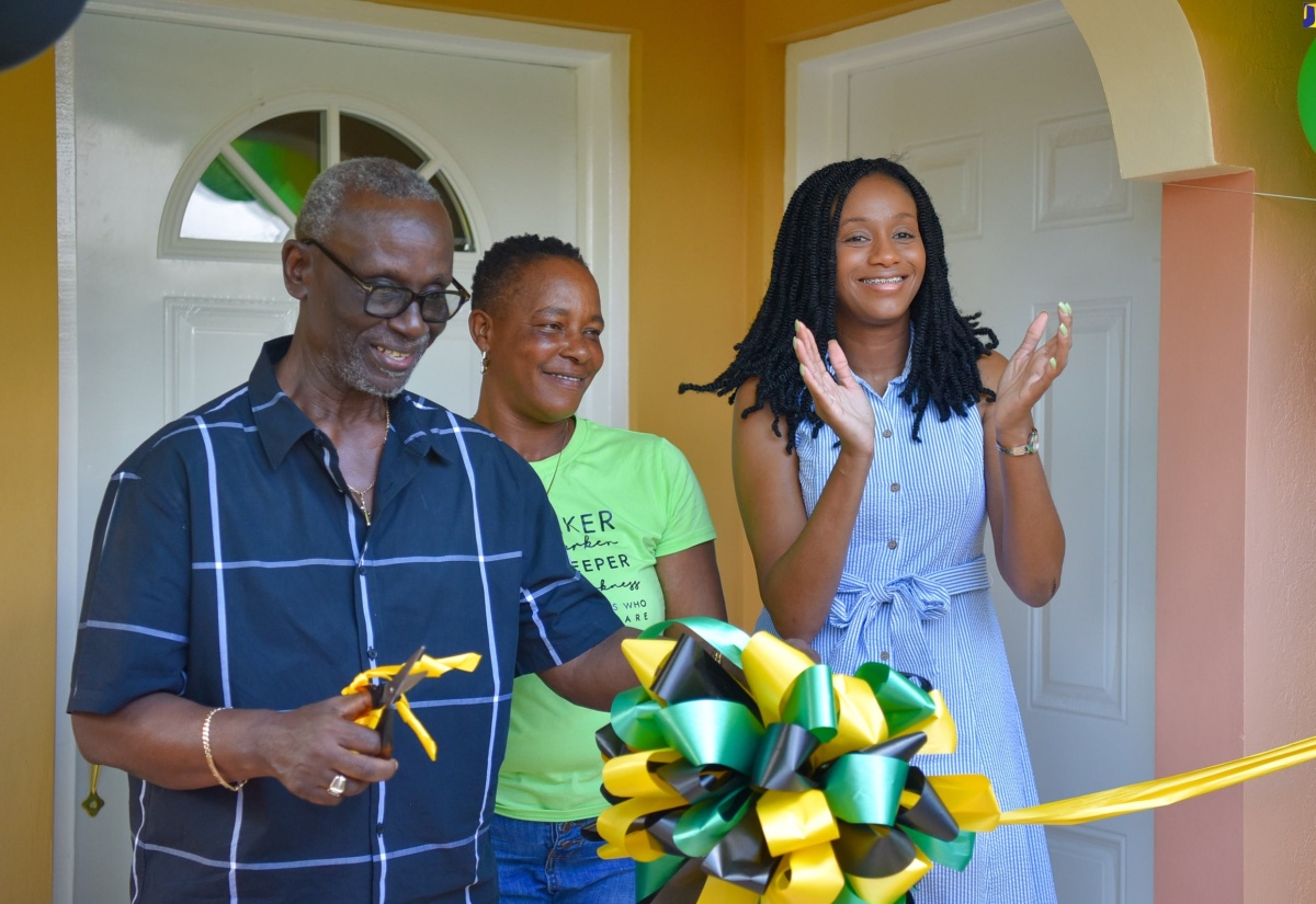 Minister of Local Government and Community Development, Hon. Desmond McKenzie, cuts the ribbon symbolising the formal handover of a two-bedroom house in Kendal, Manchester, to recipient, Nadine Lawrence (centre). The presentation was made on Friday (December 1). Applauding is Manchester Central Member of Parliament, Rhoda Moy Crawford. The unit was facilitated under the Local Government Ministry’s Indigent Housing Programme and is in keeping with the Administration’s thrust to provide homes for more Jamaicans.