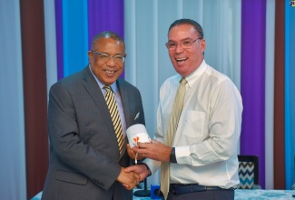 Minister of Science, Energy, Telecommunications and Transport, Hon. Daryl Vaz (right), symbolically presents a solar lamp to St. Andrew Western Member of Parliament (MP), Anthony Hylton, at the Ministry’s Maxfield Avenue offices in Kingston on Tuesday (December 12). The Government is providing 10,000 solar lamps to households across the island under a pilot project. The lamps will be distributed by MPs.

