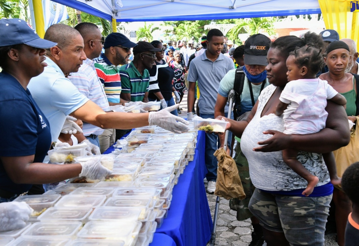 Mayor of Kingston, Senator Councillor Delroy Williams (second left), hands a cooked meal to a woman during the  Mayor’s annual New Year’s Day feeding of the homeless across the Corporate Area on Monday (January 1). The activity was held at the St. William Grant Park, downtown Kingston. Assisting at left is Brand Coordinator at Pepsi, Yanique Dawkins.

