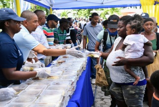 Mayor of Kingston, Senator Councillor Delroy Williams (second left), hands a cooked meal to a woman during the  Mayor’s annual New Year’s Day feeding of the homeless across the Corporate Area on Monday (January 1). The activity was held at the St. William Grant Park, downtown Kingston. Assisting at left is Brand Coordinator at Pepsi, Yanique Dawkins.

