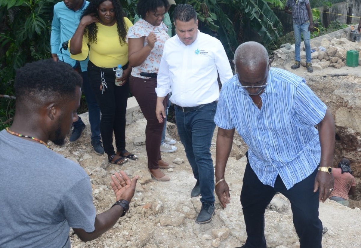 Minister of Local Government and Community Development, Hon. Desmond McKenzie (right), makes his way across a section of a broken bridge in Seville Heights, St. Ann, during a tour on Thursday (January 25). Looking on is Minister without Portfolio in the Ministry of Economic Growth and Job Creation, Senator the Hon. Matthew Samuda (second right), and other representatives from both Ministries and the St. Ann Municipal Corporation.