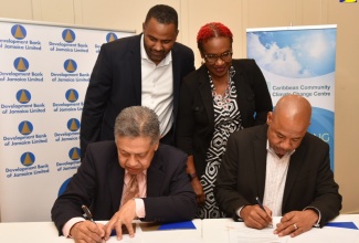 Acting Managing Director, Development Bank of Jamaica (DBJ), David Wan (seated left), and Executive Director, Caribbean Community Climate Change Centre (CCCCC), Dr. Colin Young (seated right), affix their signatures to the Memorandum of Understanding (MoU) formalising the strengthened partnership between the entities, during a ceremony at the ROK Hotel in downtown Kingston on Wednesday (February 21). Witnessing the signing (from left) are: General Manager for DBJ’s Project Management Office, Hugh Grant, and Chair, CCCCC Board of Governors,  Una May Gordon.