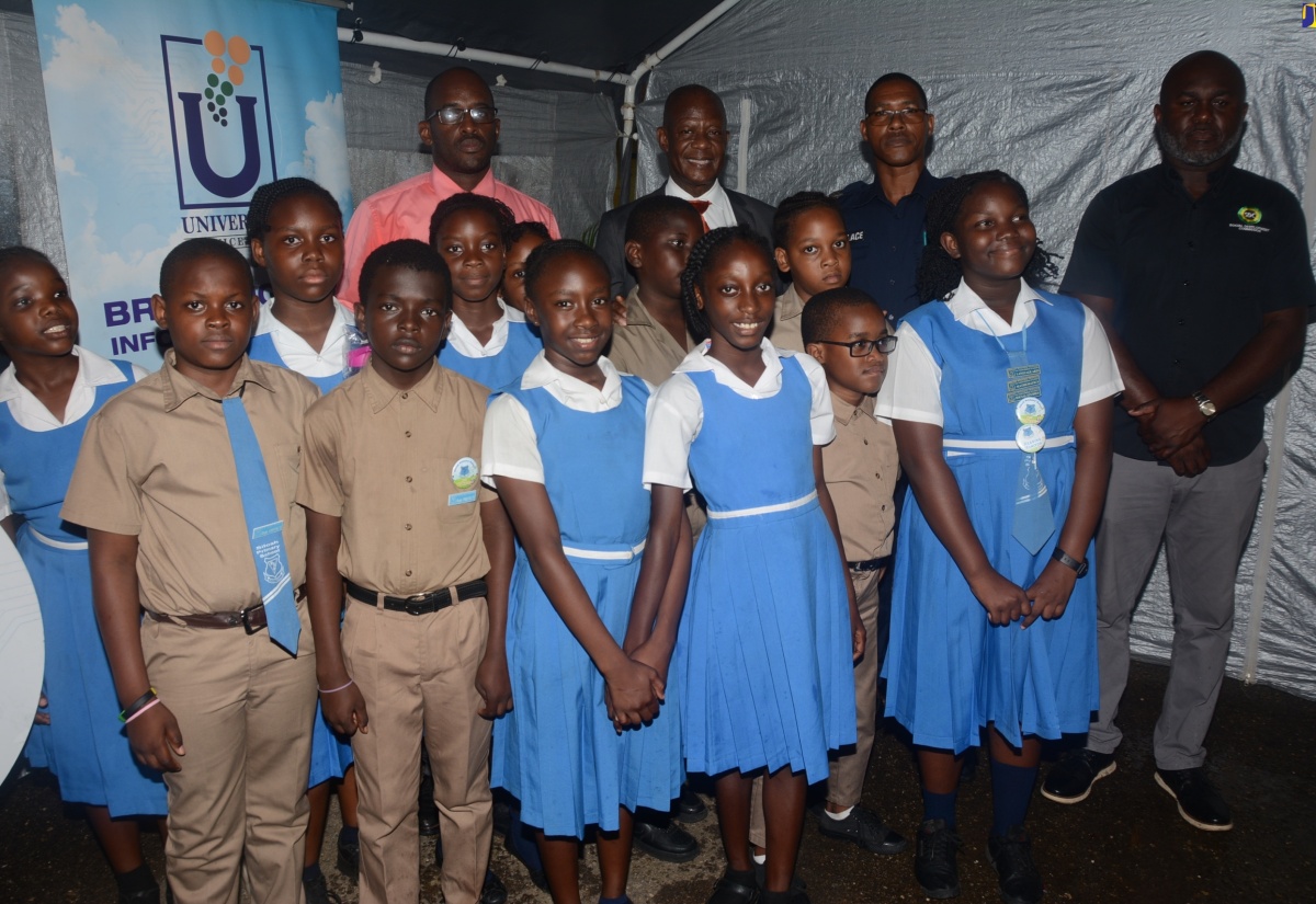 Chief Executive Officer of the Universal Service Fund (USF), Dr. Daniel Dawes (background, second left), joins students of Siloah Primary School and other stakeholders at the launch of Community Wi-Fi in Siloah, St. Elizabeth on Wednesday, March 20.  From left (in background) are Principal of the school, O’Neil Larmond; Sergeant of the Siloah Police Station, Ronnie Wallace; and Parish Manager of the Social Development Commission (SDC), Alric Miller. 