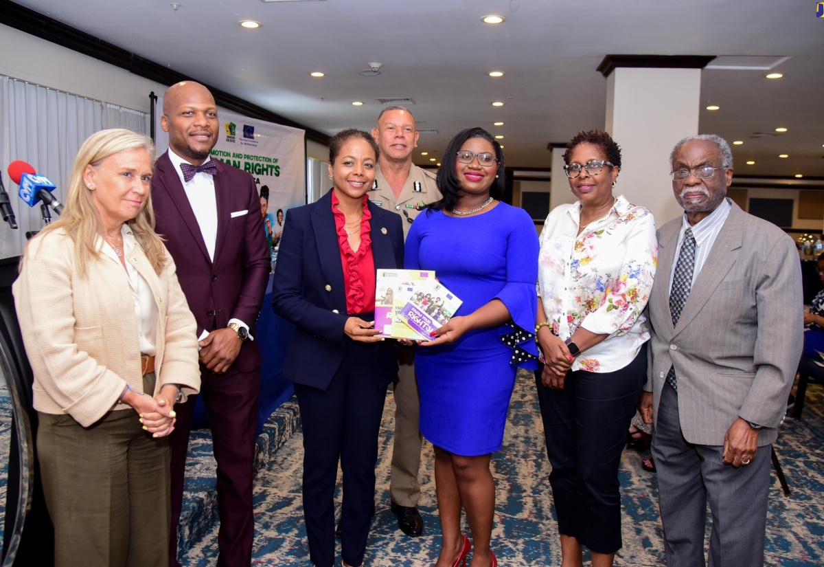 Minister of Legal and Constitutional Affairs, Hon. Marlene Malahoo Forte (third left), is presented with human rights booklets by Jamaicans for Justice (JFJ) Executive Director, Mickel Jackson, during Monday’s (April 29) JFJ-European Union (EU) Project Launch for the Promotion and Protection of Human Rights in Jamaica, at The Jamaica Pegasus hotel in New Kingston. Sharing the moment (from left) are European Union Ambassador to Jamaica, Her Excellency Marianne Van Steen; Permanent Secretary in the Ministry of Legal and Constitutional Affairs, Wayne Robertson; Deputy Police Commissioner Clifford Blake; Opposition Spokesperson on Foreign and Regional Affairs, Dr. Angela Brown-Burke, and Constitutional Law Expert, Dr. Lloyd Barnett.  