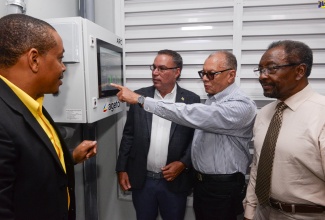 Minister of Science, Energy, Telecommunications and Transport, Hon. Daryl Vaz (second left), observes as Executive Chairman, LASCO Affiliated Companies, James Rawle (second right). Looking on (from left) are General Manager, Renewable Energy Design and Installation Services (REDIS) Limited, Kevin Mills and United States Ambassador to Jamaica, His Excellency Nick Perry. Occasion was a ceremony to celebrate the successful completion of the project held on April 11 at LASCO Distributors Limited’s plant in White Marl, St. Catherine.