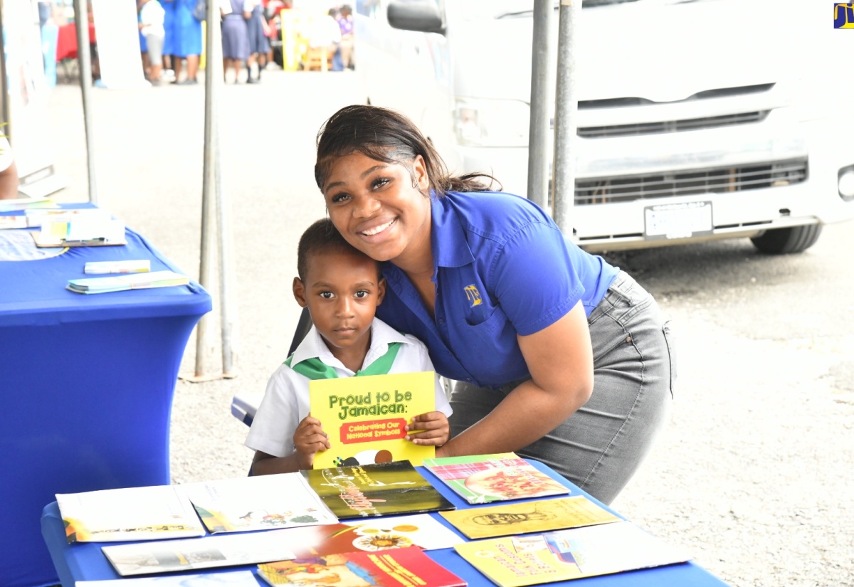  Special Projects Officer, Jamaica Information Service (JIS), Romona Geohaghan, presents a copy of the JIS publication ‘Proud To Be Jamaican’ to little Khajarie Grant, who visited the JIS booth during the St. Mary 4-H Clubs’ Parish Achievement Expo, held recently at the St. Mary High School.