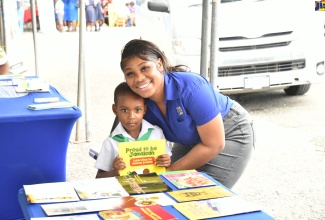  Special Projects Officer, Jamaica Information Service (JIS), Romona Geohaghan, presents a copy of the JIS publication ‘Proud To Be Jamaican’ to little Khajarie Grant, who visited the JIS booth during the St. Mary 4-H Clubs’ Parish Achievement Expo, held recently at the St. Mary High School.