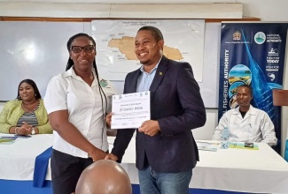 Minister of Agriculture, Fisheries and Mining, Hon. Floyd Green, presents a certificate to Nicholette Shaw, a fisher of Discovery Bay Fisherman’s Beach, St. Ann,  for participating in training in horizontal line fishing.  Ms. Shaw was among 40 fishers presented with certificates at the Discovery Bay Marine Laboratory in the parish on April 17. Seated (from left) are Senior Operations Analyst at the World Bank – Caribbean , Jhanelle-Rae Bowie and Principal Director of the National Fisheries Authorities (NFA), Stephen Smikle .

