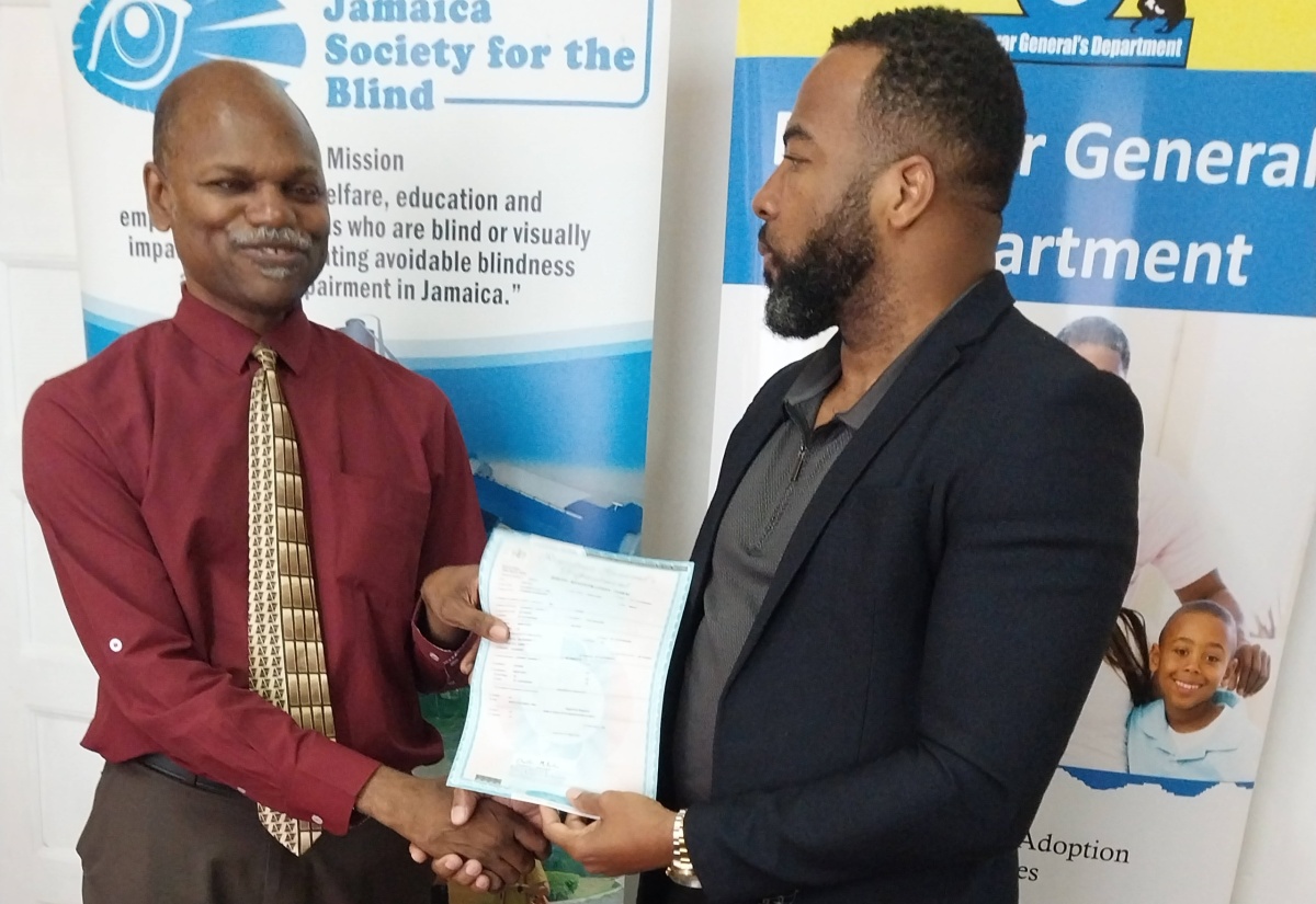 Former Chief Executive Officer, Registrar General's Department (RGD), Charlton McFarlane (right), presents Executive Director, Jamaica Society for the Blind, Conrad Harris, with a Braille birth certificate  at the official launch on May 1, at the offices of the Jamaica Society for the Blind in Kingston.