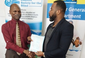 Former Chief Executive Officer, Registrar General's Department (RGD), Charlton McFarlane (right), presents Executive Director, Jamaica Society for the Blind, Conrad Harris, with a Braille birth certificate  at the official launch on May 1, at the offices of the Jamaica Society for the Blind in Kingston.