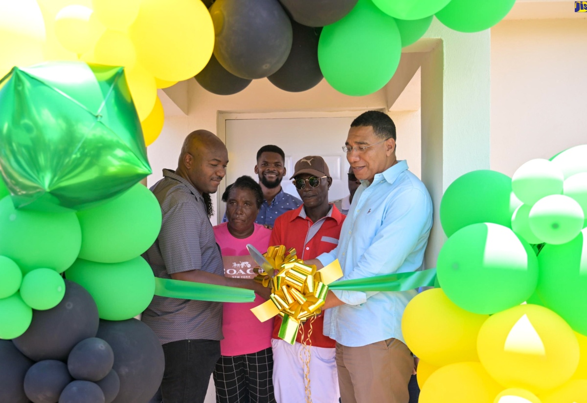 Prime Minister, the Most Hon. Andrew Holness (right), cuts the ribbon to handover a home under the New Social Housing Programme (NSHP), to Gerald McKenzie (second right) in Race Course, Clarendon on Friday (May 24). Others sharing in the occasion from left are: Member of Parliament for Clarendon South Western, Lothan Cousins, and Mr. McKenzie’s spouse, Verna Redhi.