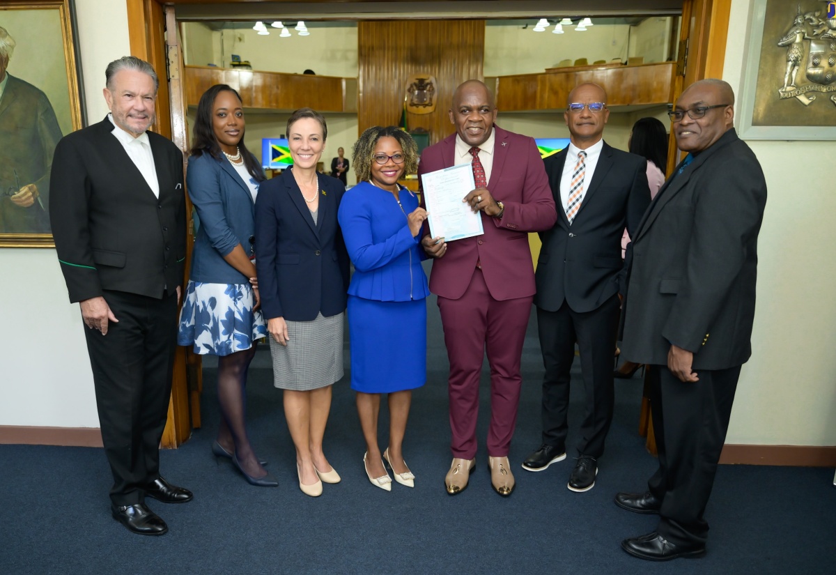 Minister Without Portfolio in the Office of the Prime Minister with Responsibility for Skills and Digital Transformation, Senator Dr. the Hon. Dana Morris Dixon (centre), presents Opposition Senator, Dr. Floyd Morris (third right) with a copy of his birth certificate in Braille during a brief ceremony before the start of the sitting of the Senate at Gordon House on Friday (May 10). Others sharing the moment (from left) are President of the Senate, Senator Tom Tavares-Finson; Clerk to the Houses of Parliament, Colleen Lowe; Minister of Foreign Affairs and Foreign Trade, Senator the Hon. Kamina Johnson Smith; Opposition Senator, Peter Bunting; and Acting Chief Executive Officer, Registrar General's Department (RGD), Desmond Davis.

