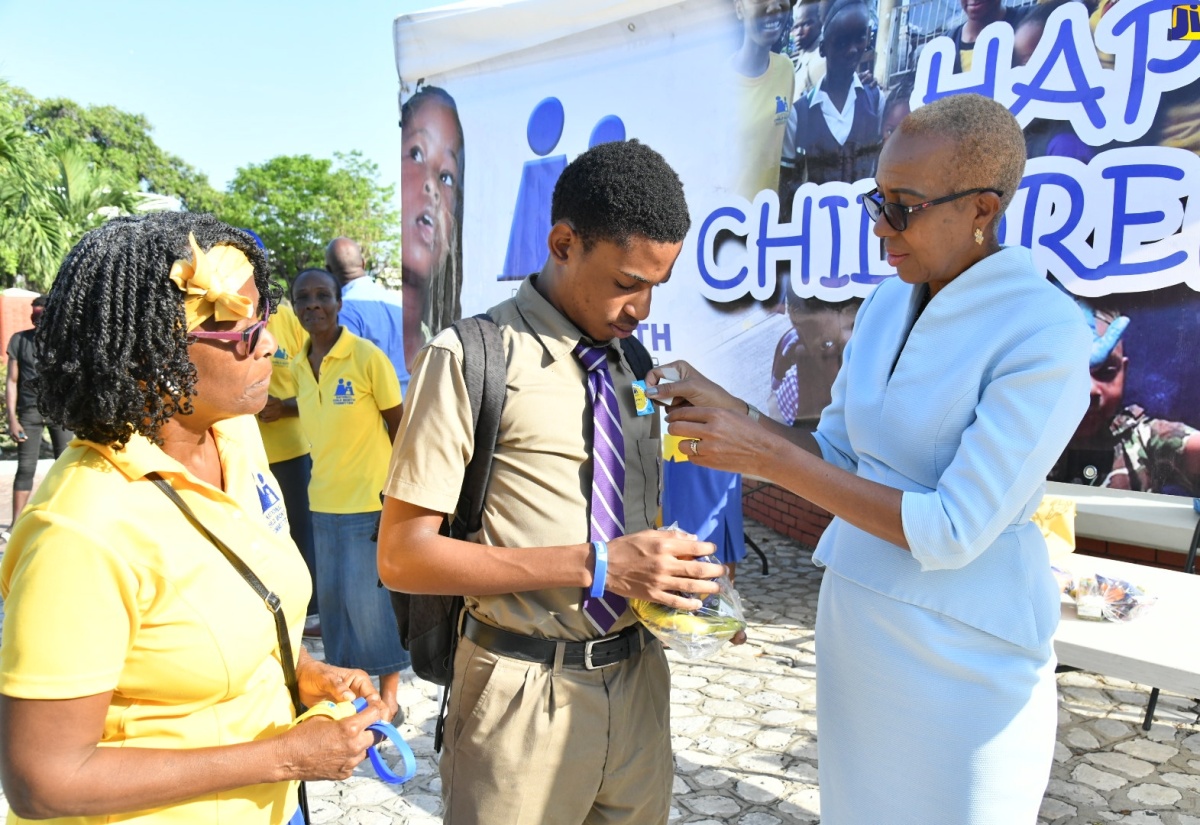 Minister of Education and Youth, Hon. Fayval Williams (right), places a sticker on Kingston College student, Ricquan Bailey, as part of activities marking Children’s Day at St. William Grant Park in downtown Kingston on Friday (May 17). The event was organised by the National Child Month Committee (NCMC). Looking on is NCMC Chair Emeritus, Dr. Pauline Mullings.

