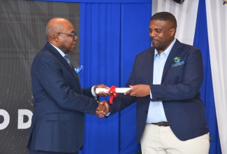 Minister of Tourism, Hon. Edmund Bartlett- (left) makes a presentation to Founder, Caribbean Front Desk and winner of the inaugural Tourism Innovation Incubator pitch event, Dr. Duane Chambers at the initiative’s closing ceremony last year at the Summit in Kingston.