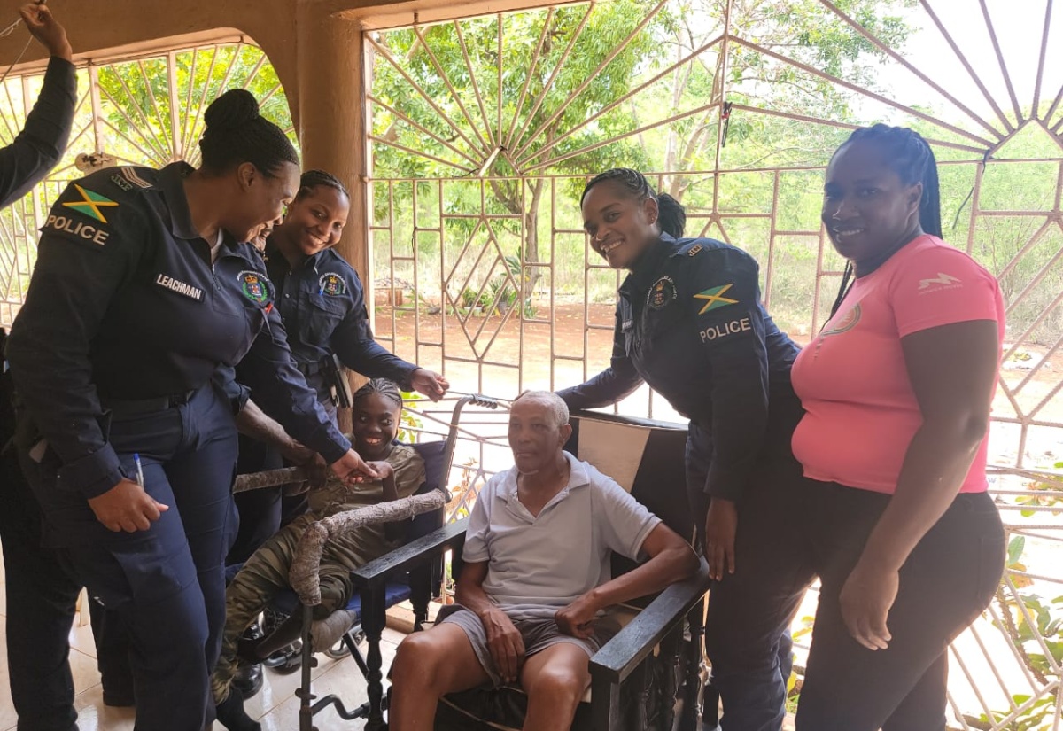 Head of the Guanaboa Vale Police, Sergeant Navelette Davis-Leachman (left); office attendant at the station, Glacier Maxwell (right), along with other officers from the station, interact with resident of the St. Catherine-based Rock of Hope Residential Manor, James Mitchell (seated), on Labour Day (May 2023).

