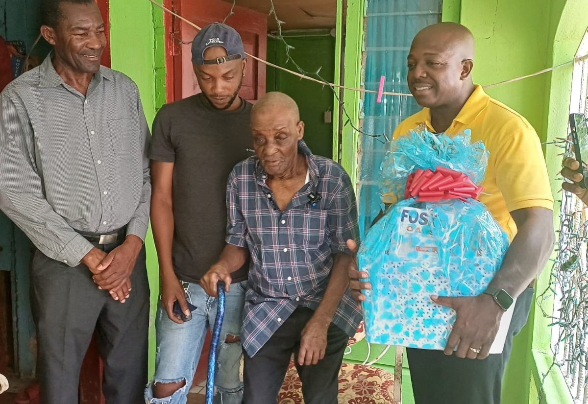 Minister of Labour and Social Security, Hon. Pearnel Charles Jr. (right), visits with Jamaica’s second oldest living person on record, 109-year-old Uton Samuels (second right), at his residence in Green Island, Hanover, on May 17. The occasion of Mr. Charles visit was to present Mr. Samuels with a gift basket as part of the Ministry’s activities to mark Centenarians’ Day on Monday (May 20). Sharing the moment are (from left) Manager for the Ministry’s Hanover parish office, Devon Malcolm, and Mr. Samuels’ grandson, Everton Neil.

