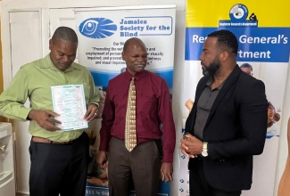 Chairman of the Jamaica Society for the Blind (JSB), Daemion McLean (left), displays a copy of one of the first printed Braille birth certificates that were presented to the Society on May 1, 2024. Also sharing the moment are the JSB’s Executive Director, Conrad Harris (centre) and former Chief Executive Officer and Deputy Keeper of Records at the Registrar General’s Department, Charlton McFarlane.

