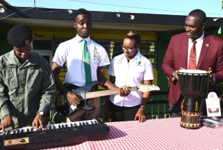 Minister of State in the Ministry of National Security, Hon. Juliet Cuthbert Flynn (second right), looks on as Head Boy at Old Harbour High School in St. Catherine, Acado Brown (second left), strums an electric guitar that was among several musical instruments she handed over to the institution during a brief ceremony on Monday (May 27). Others (from left) are Old Harbour High student, Tevin Scott, and Principal, Lynton Weir.

