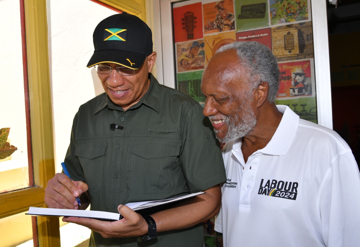 Prime Minister, the Most Hon. Andrew Holness (left), signs the guest book following a tour of the Jamaica Music Museum by Director/Curator, Jamaica Music Museum, Herbie Miller (right), today (May 23) in downtown Kingston.