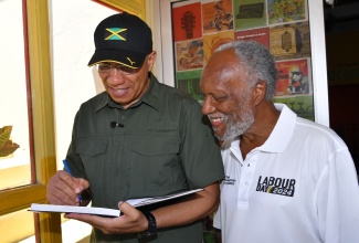 Prime Minister, the Most Hon. Andrew Holness (left), signs the guest book following a tour of the Jamaica Music Museum by Director/Curator, Jamaica Music Museum, Herbie Miller (right), today (May 23) in downtown Kingston.