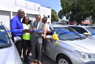 Managing Director at the Transport Authority, Ralston Smith (second right), cuts the ribbon to officially hand over 12 motor vehicles during a ceremony held at the Authority’s Maxfield Avenue offices in Kingston, on April 25. Others (from left) are Board Chairman, Transport Authority, Owen Ellington; new recruit at the Authority, Melissa Duncan; and Driver, Clovis Ashmede.