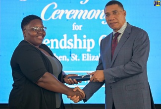 Prime Minister, the Most Hon. Andrew Holness, presents land title to beneficiary, Shashana Atkinson, during the official handover of residential serviced lots at the new Friendship Oaks Phase 1 development in Goshen, St. Elizabeth, on Friday (May 17).

