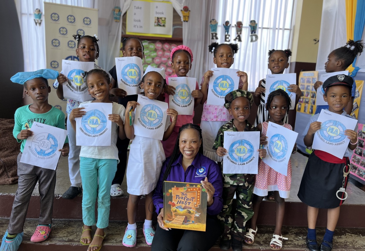 Students from St. Joseph’s Infant School in Kingston display  the National Land Agency's logo during Read Across Jamaica Day on May 7.  Seated is the  Agency’s Manager of Marketing and Public Relations, Nicole Hayles, who read to the students.


