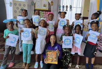 Students from St. Joseph’s Infant School in Kingston display  the National Land Agency's logo during Read Across Jamaica Day on May 7.  Seated is the  Agency’s Manager of Marketing and Public Relations, Nicole Hayles, who read to the students.

