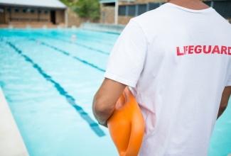 Rear view of lifeguard standing with rescue buoy near poolside