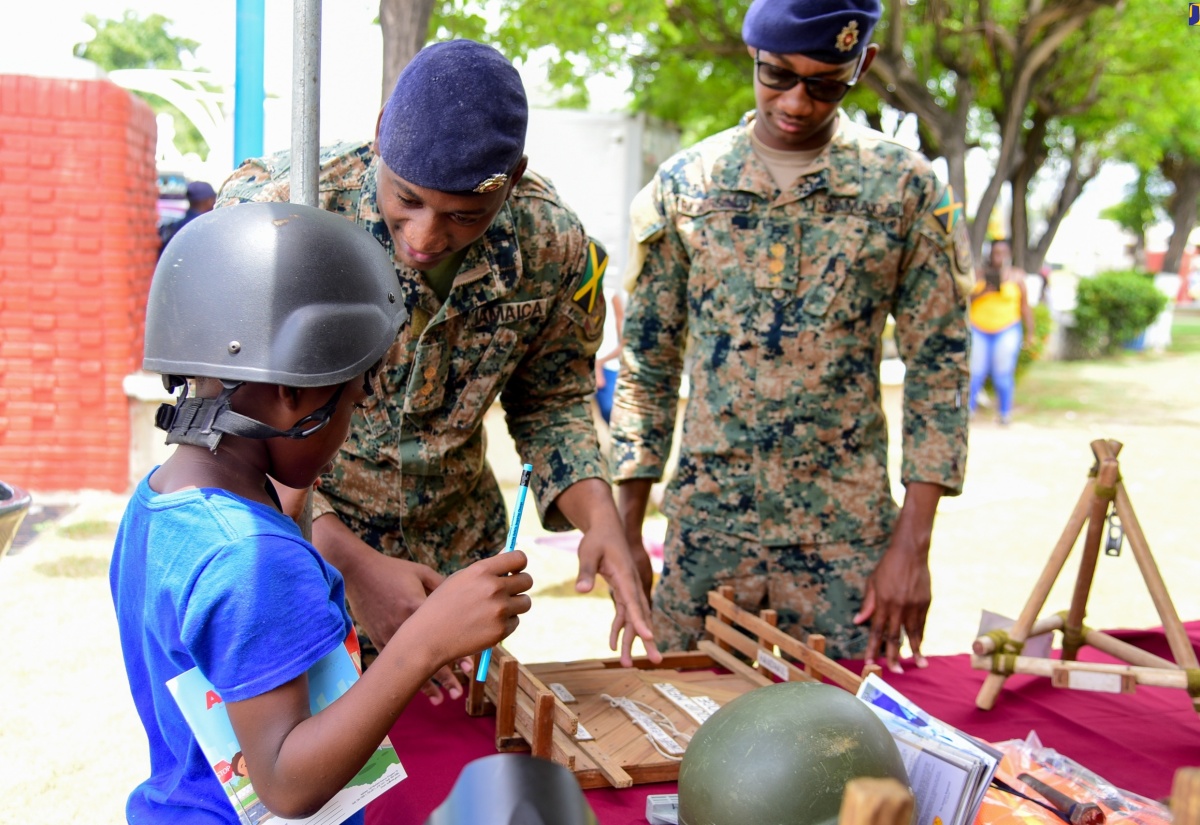 Lieutenant Kyle-Anthony Mundell (centre) of the Jamaica Defence Force, explains the roles and functions of combat engineers to a curious young patron at the Kingston and St. Andrew Municipal Corporation (KSAMC) All Hazards Expo and Emergency Cook-Off, held at the St. William Grant Park, downtown Kingston on Friday June 21. Looking on is Lieutenant Rojae Pickersgill.