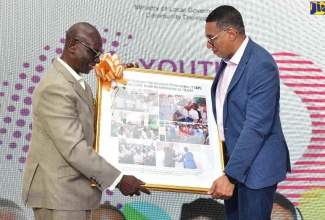 Prime Minister, the Most Hon. Andrew Holness (right), accepts a token of appreciation from Minister of Local Government and Community Development, Hon. Desmond McKenzie, during the official launch of the 2024 Youth Summer Employment Programme (YSEP) at the William Knibb Memorial High School in Trelawny on Friday (June 28).