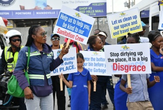 MPM Waste Management Limited staff are joined by students in displaying signs promoting environmental responsibility during an environmental awareness march from Red Hills Mall to Swallowfield Primary in Kingston on June 4. The event, held in observance of National Environmental Awareness Week from June 1-8, involved Swallowfield Primary School students, Social Development Commission (SDC) representatives, and White Hall Community Development Committee (CDC) members.