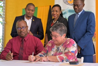 Papine High School Principal, Leighton Christie (seated left), looks on as General Manager, Jamaica Bauxite Institute (JBI), Yolanda Drakapoulos, signs a Memorandum of Understanding (MOU) for the use of a greenhouse owned by the JBI for the advancement of the school’s agriculture programme. The ceremony was held on June 14 at the JBI’s offices in St. Andrew where the greenhouse is situated. Looking on are (from left) Minister of Agriculture, Fisheries and Mining, Hon. Floyd Green; State Minister in the Ministry of Education and Youth, Hon. Marsha Smith; and Board Chair of the Papine High School, Dr. Noel Watson.

