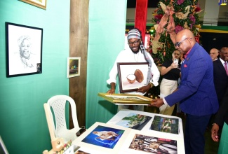 Tourism Minister, Hon. Edmund Bartlett (right), admires a canvas painting by artist Delroy Millwood (left). Occasion was the opening of the two-day Christmas in July trade show on July 11, at the National Arena.

