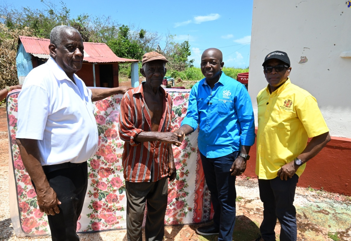 Minister of Labour and Social Security, Hon. Pearnel Charles Jr. (second right) hands over a mattress to resident of Tryall, Nascius Powell (second left), during a tour of communities in southern St. Elizabeth on July 12. Looking on (from left) are State Minister in the Ministry of Agriculture, Fisheries and Mining, Hon. Franklin Witter and Minister of State in the Ministry of Labour and Social Security, Dr. the Hon. Norman Dunn. 