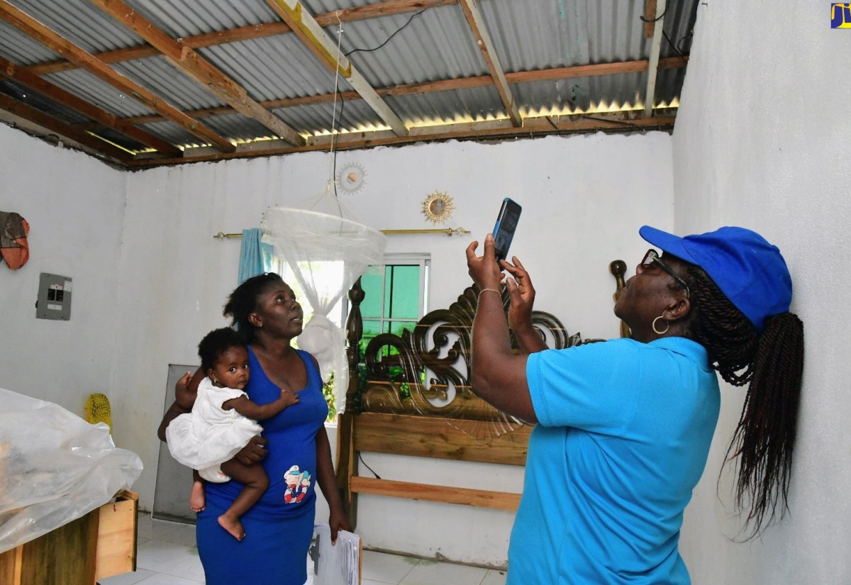 Social Worker, Ministry of Labour and Social Security, Clurdine Powell Harrison, uses a mobile phone to capture images highlighting damage to Cameka Chamberlin's residence in Mitchell Town, during the passage of Hurricane Beryl on July 3. Occasion was a visit to the community in Clarendon on July 10 by teams from the Ministry to assess the damage and provide relief items to the affected residents.

