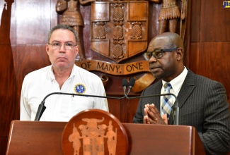 Minister of Science, Energy, Telecommunications and Transport, Hon. Daryl Vaz (left), listens as Director General of the Office of Utilities Regulation (OUR), Ansord Hewitt, addresses Wednesday's (July 31) post-Cabinet press briefing at Jamaica House.