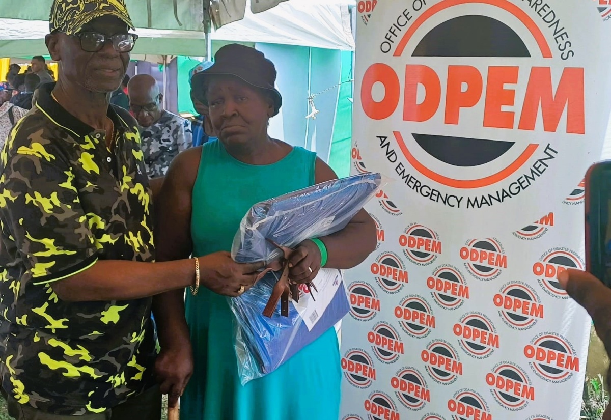 Minister of Local Government and Community Development, Hon. Desmond McKenzie (left), hands over hurricane straps and a tarpaulin to Pearl Drummond from Crawford in St. Elizabeth. Occasion was the Ministry’s Hurricane Roof Strap Expo held at the JAG Myers Park in Black River on Friday (July 26).