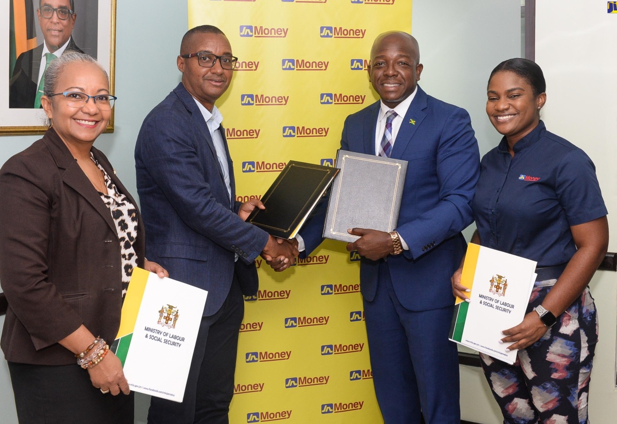 Minister of Labour and Social Security, Hon. Pearnel Charles Jr. (second right), and General Manager of Jamaica National Money Services, Horace Hines (second left), display signed copies of a Memorandum of Understanding (MOU) that will strengthen the support provided to seasonal workers in Canada. Sharing in the occasion (from left) are Permanent Secretary in the Ministry, Collette Roberts Risden; and Marketing and Sales Manager at Jamaica National Money Services, Cedrica Reid. The MOU was signed on Tuesday (July 23) at the Ministry’s North Street offices in Kingston.

