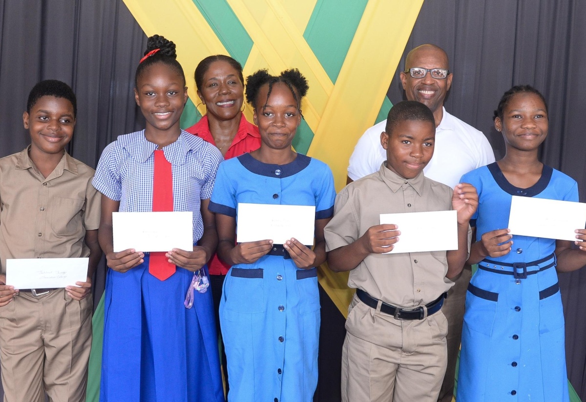 Students from St. Catherine display scholarship cheques from the Poverty Alleviation and Empowerment Foundation (PAEF), which were presented on Wednesday (July 24), at the Parish Office of the Social Development Commission (SDC) in Spanish Town. Sharing the moment are Executive Director of the PAEF, Pauline Gregory-Lewis (background, left)), and Chairman of the Foundation, Devon Samuels (background, right).

