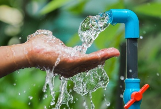 Hand under flowing water from blue outdoor faucet. 