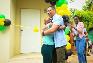 Prime Minister, the Most Hon. Andrew Holness (right), is warmly hugged by North Central Clarendon’s Beverly Howell, after she received the keys to her new one-bedroom home under the Government’s New Social Housing Programme on Friday (August 2).
