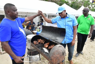 Minister of Agriculture, Fisheries and Mining, Hon. Floyd Green (right) greets jerk vendor Joseph Brown during the recent staging of the Pagee Fisherman’s Regatta at the Pagee Beach, Port Maria, St. Mary.

