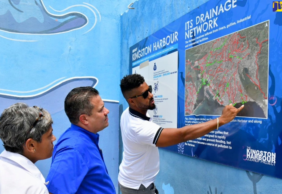 Minister without Portfolio in the Ministry of Economic Growth and Job Creation, Senator the Hon. Matthew Samuda (centre), and Consultant for the Kingston Cleanup Project, Deika Morrison (left), are shown the layout of the drainage network for the Kingston Harbour by Managing Director, Clean Harbours Jamaica Limited, Michael McCarthy. The occasion was a tour of interceptor barriers at Barnes Gully, along Port Royal Street in downtown Kingston on Thursday (August 22).

